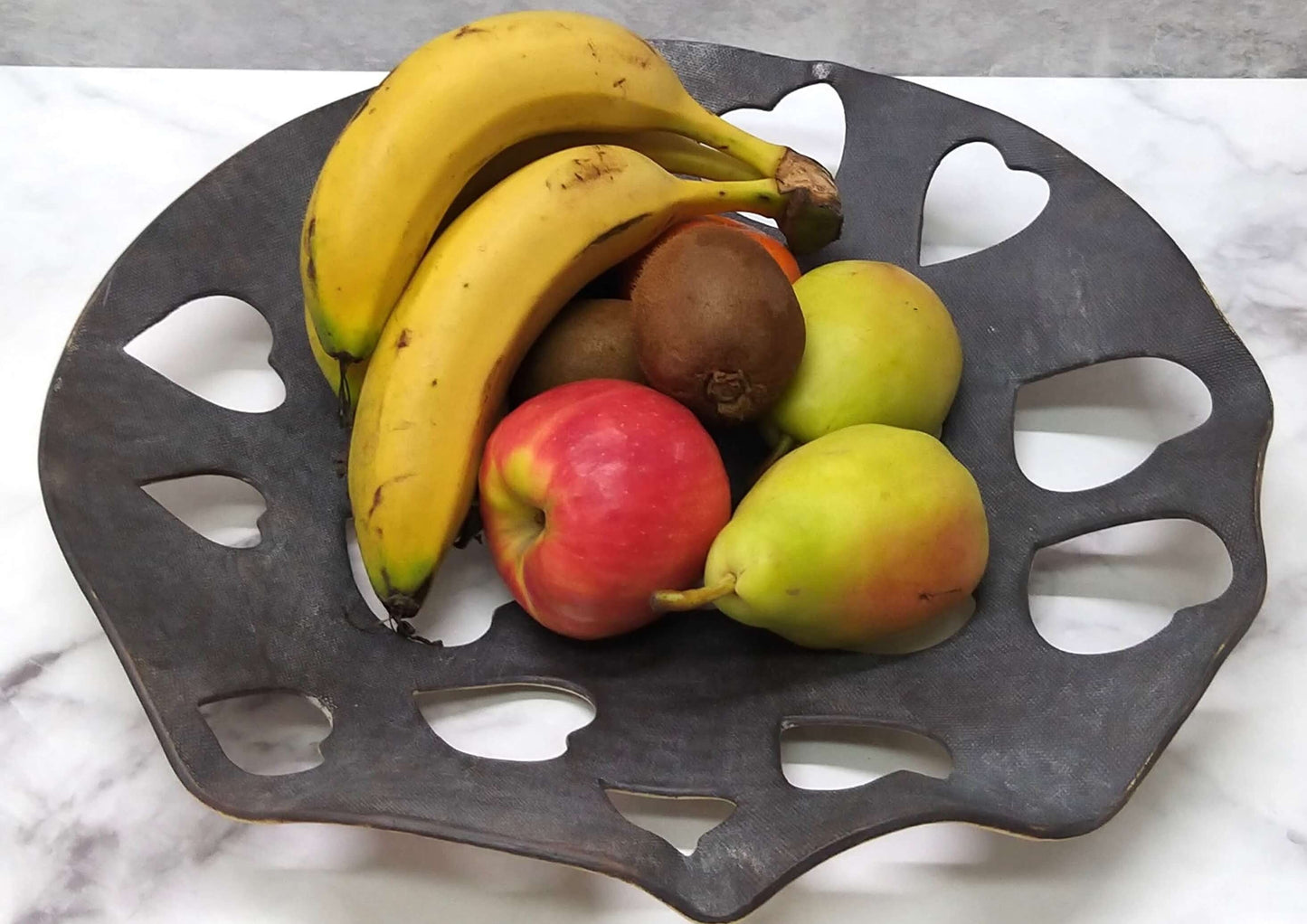 Dark ceramic Valentine’s bowl filled with fruits and large heart holes in sparse pattern