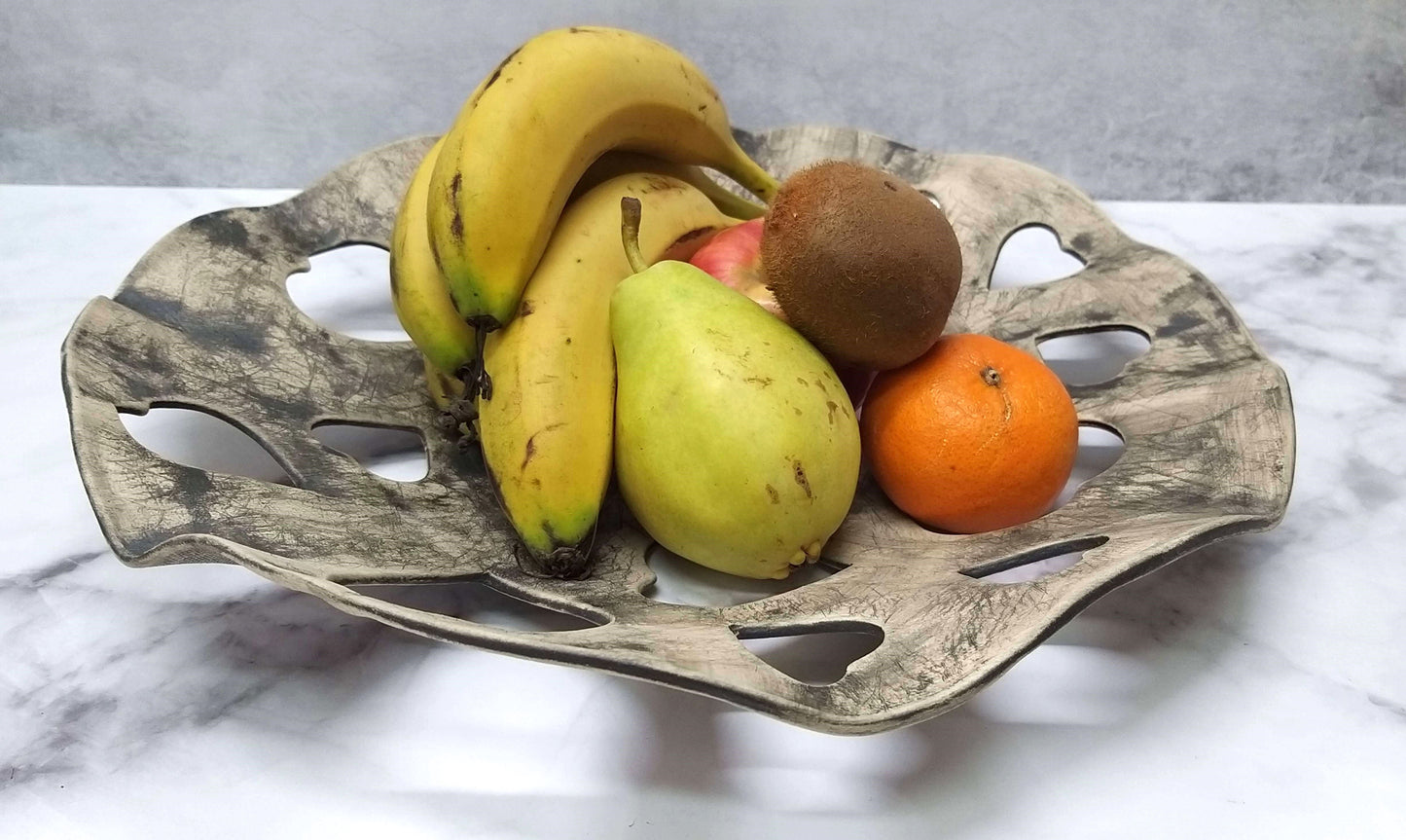 Decorative gray bowl with fruits placed in lattice of black heart-shaped holes