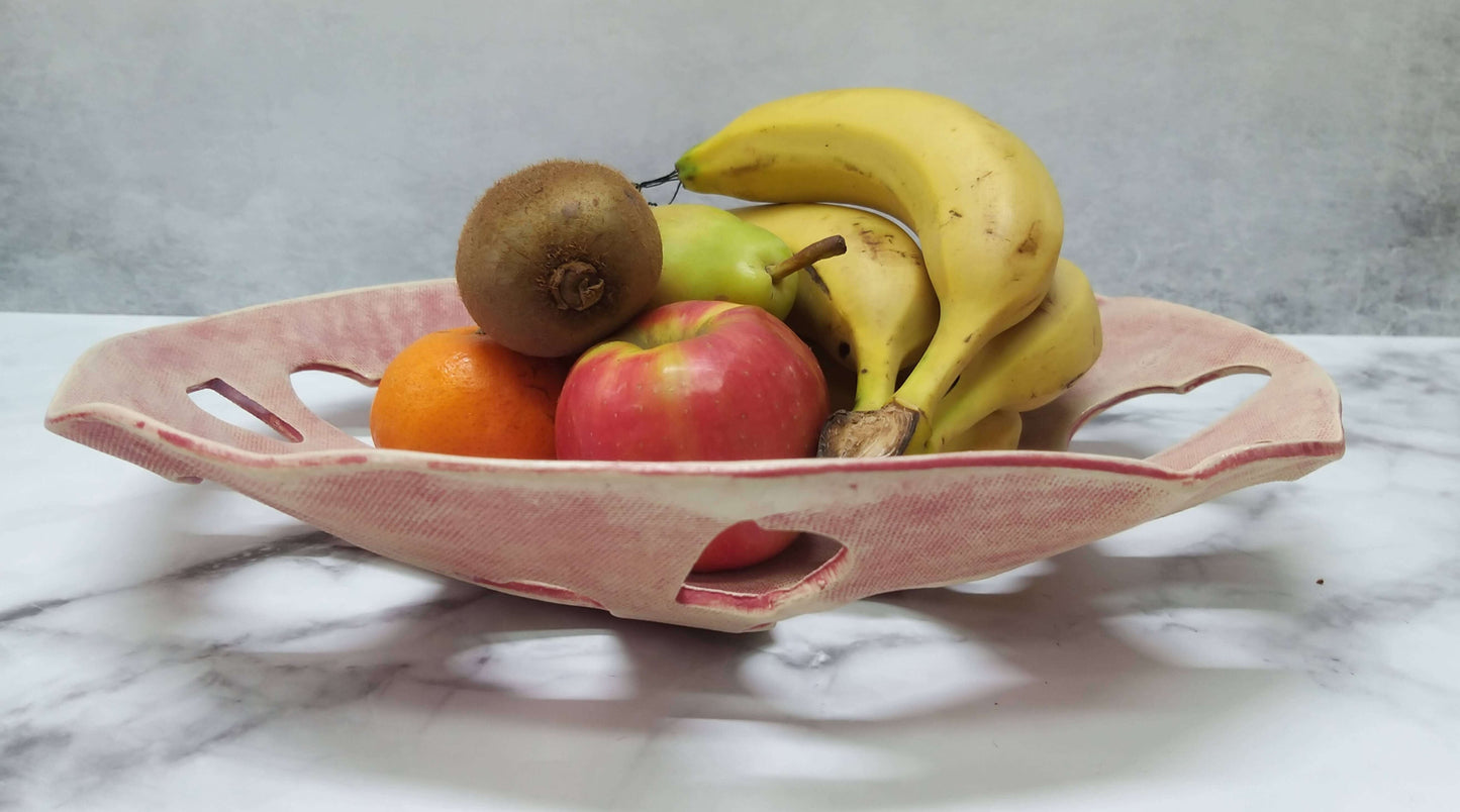 Heart-shaped perforations form lattice design on bright red bowl displayed with fruits