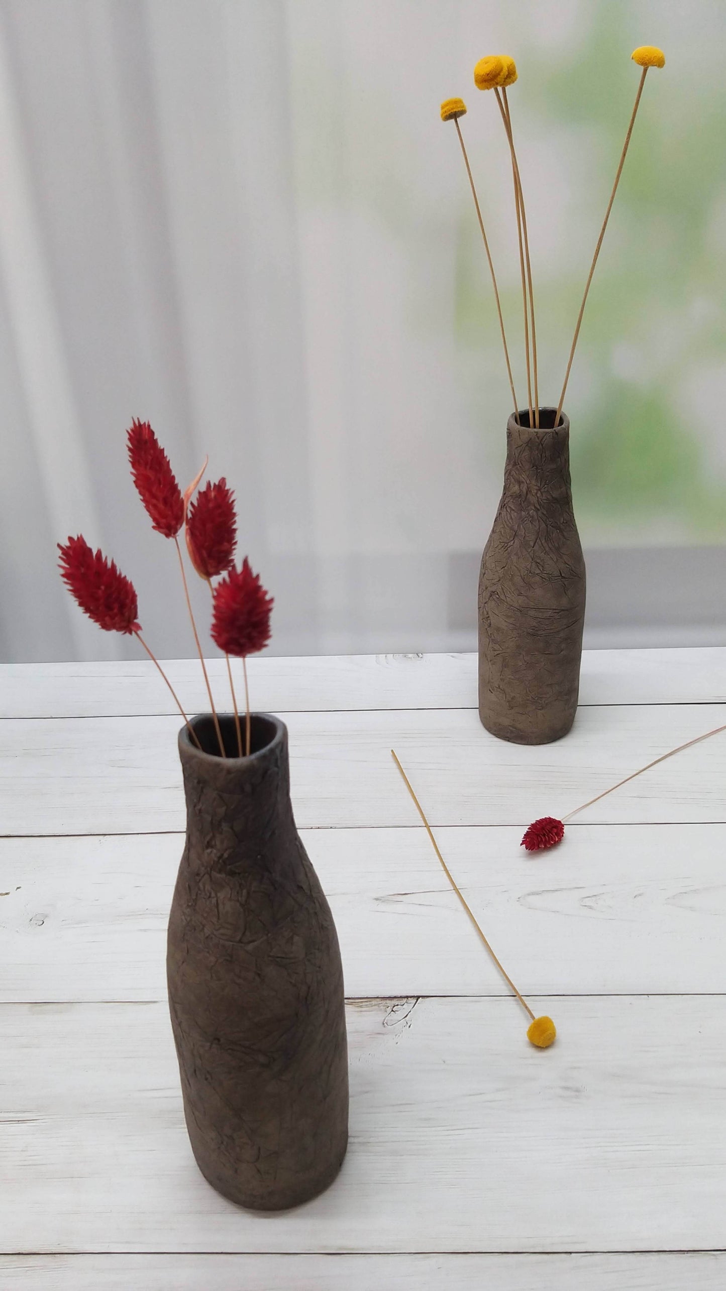 Two dark gray bottle-shaped vases are placed next to each other with red and yellow flowers inside