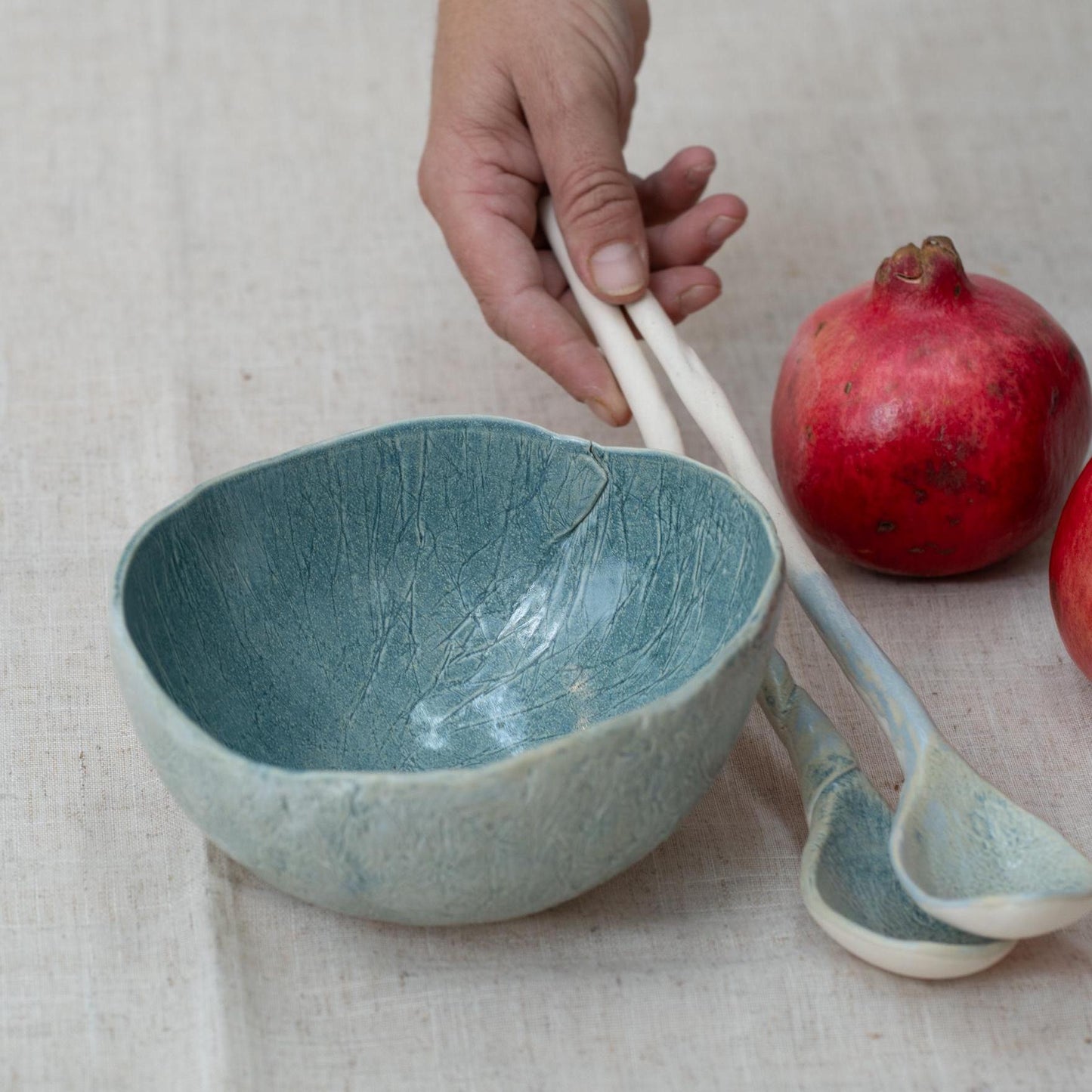 Ceramic bowl and spoon with a pomegranate on a textured surface