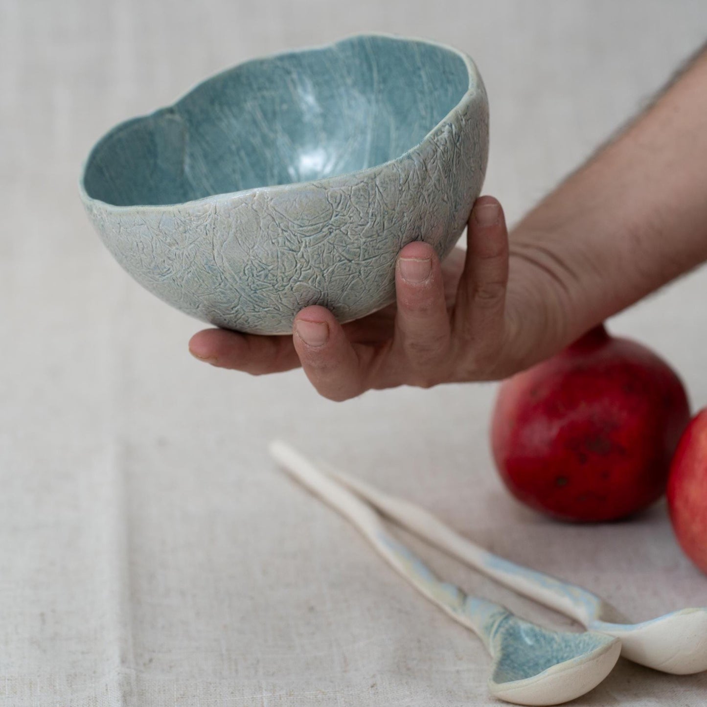 Hand holding a textured ceramic bowl with pomegranates and a spoon in the background