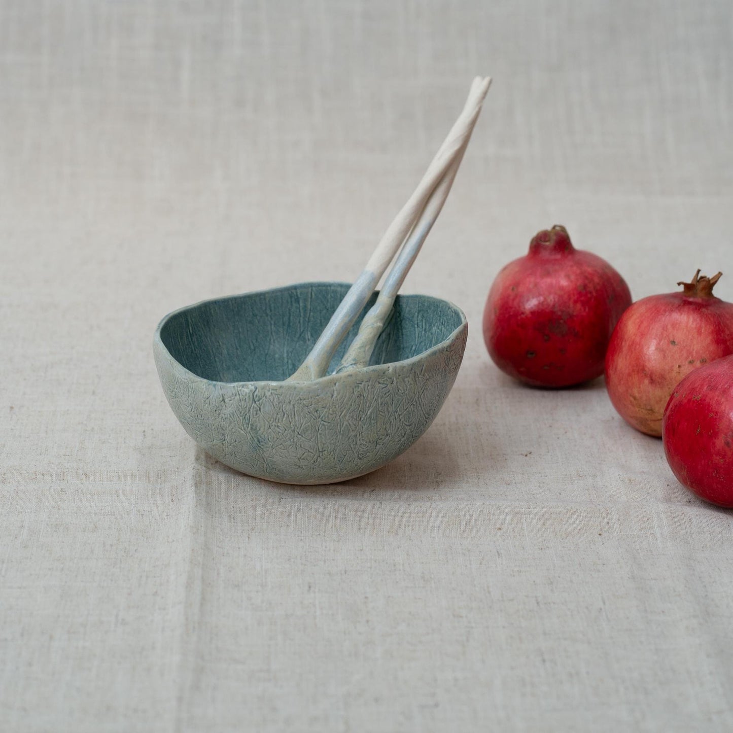 Blue ceramic bowl with two spoons and pomegranates on a textured surface
