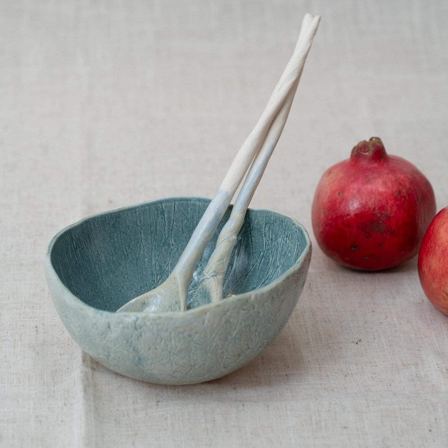 Blue ceramic bowl with two ceramic spoons and pomegranates on a light background