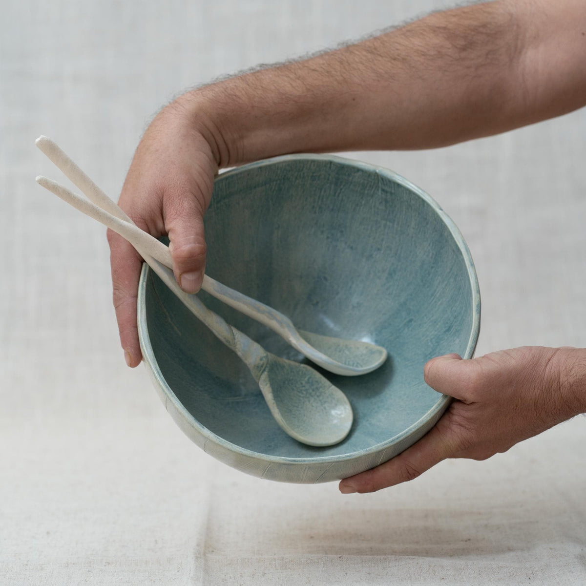 Person holding a blue ceramic bowl with two blue spoons on a light background