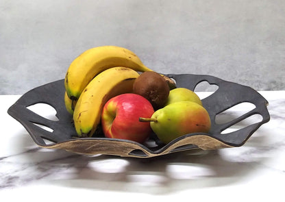 Heart-shaped perforations form lattice design on black metalic bowl displayed with fruits
