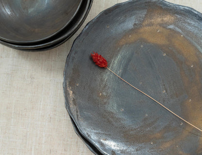 Handmade black ceramic plate next to a rustic bowl