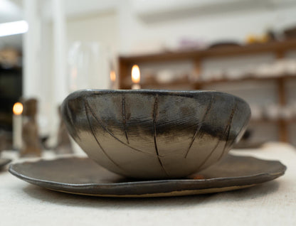 Close-up of handmade black ceramic bowl on rustic plate


