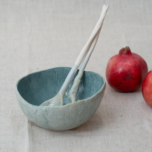 Blue ceramic bowl with two ceramic spoons and pomegranates on a light background
