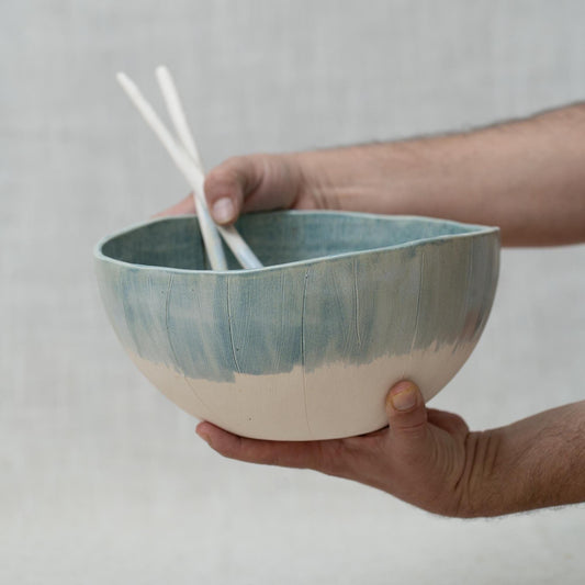 Hand holding a ceramic bowl with a gradient design against a plain background
