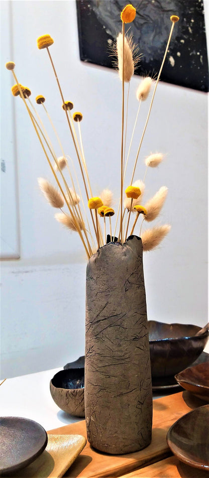 A gray ceramic vase with dried yellowish flowers is placed on a table