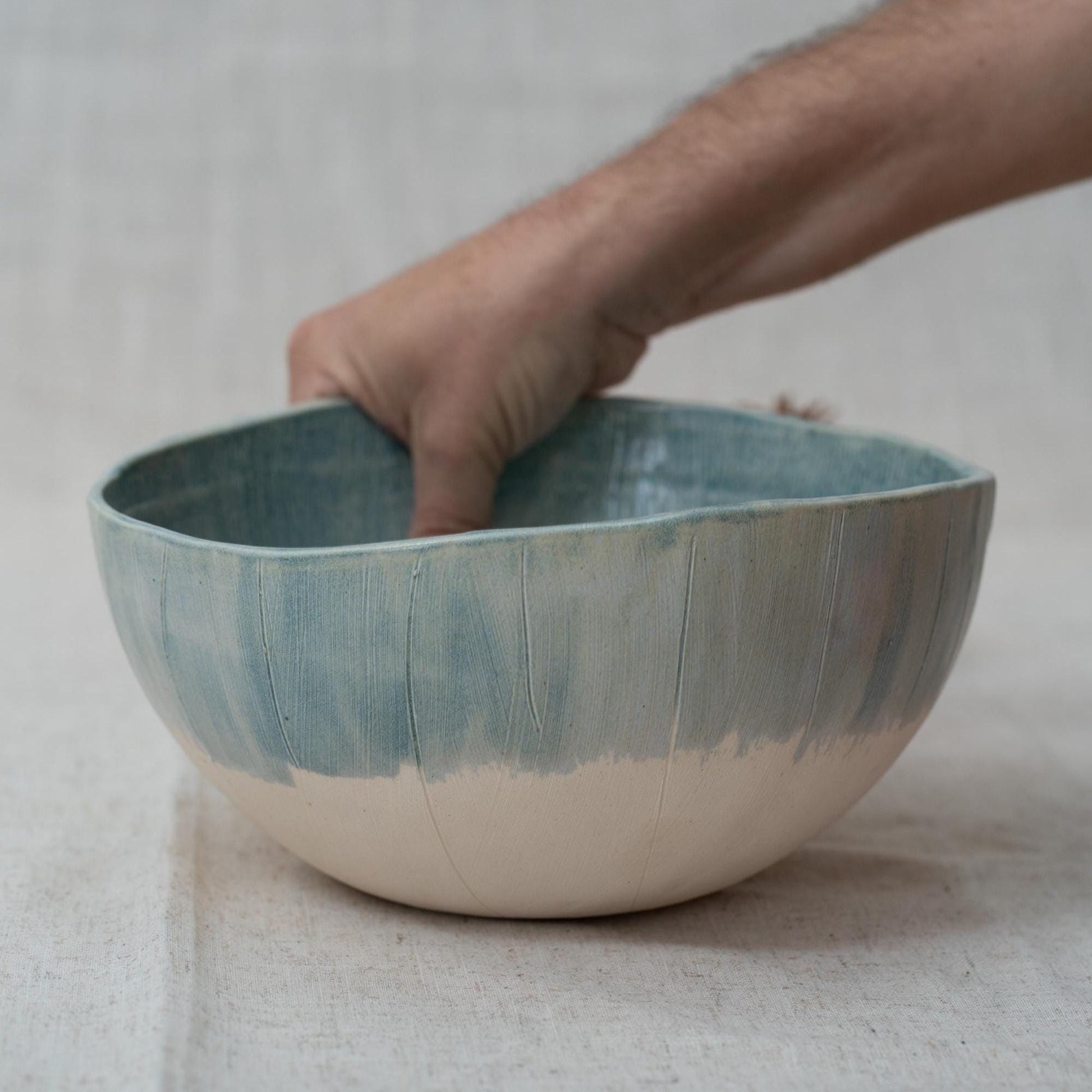 Hand holding a ceramic bowl with a textured surface on a neutral background