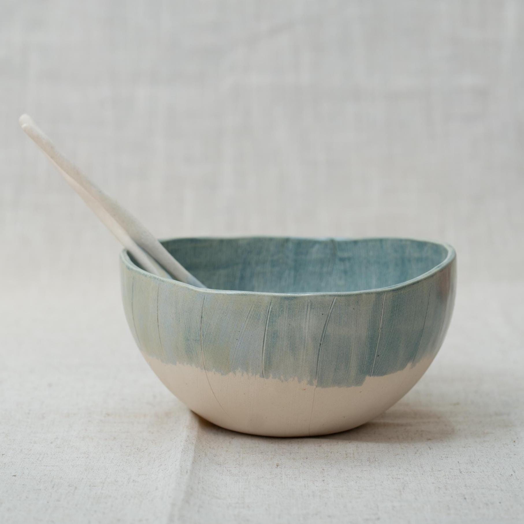 Blue ceramic bowl with two ceramic spoons on a light gray background