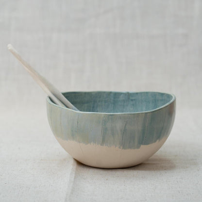 Blue ceramic bowl with two ceramic spoons on a light gray background