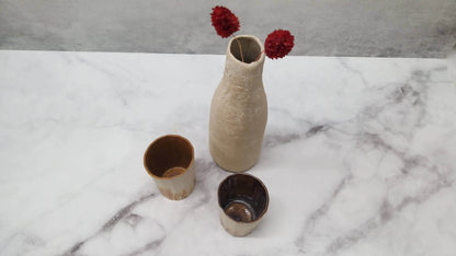 white botle-shape vase with red flowers and two espresso cups