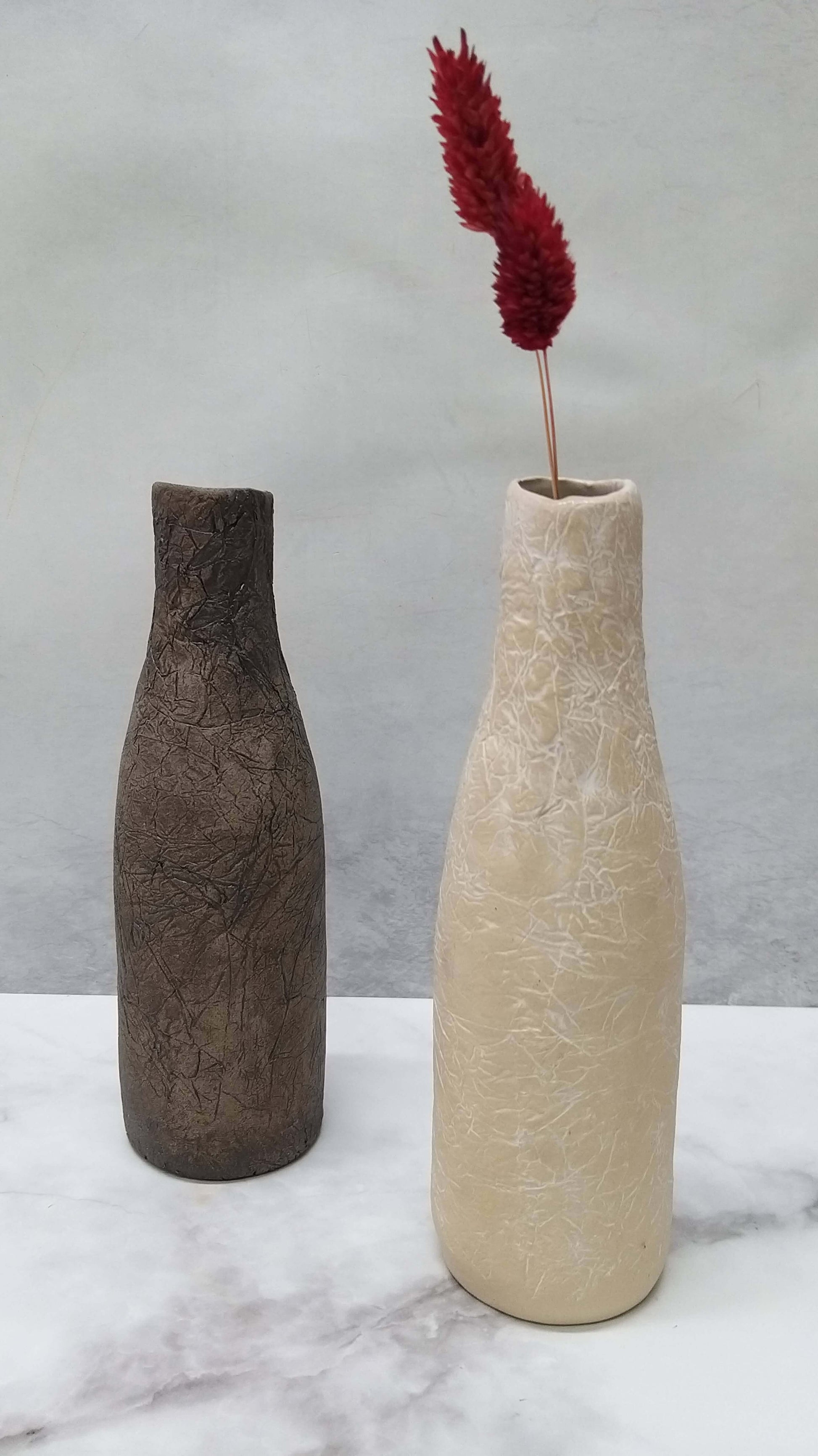 black ceramic vase and whote ceramic vase with red flowers in the white vase